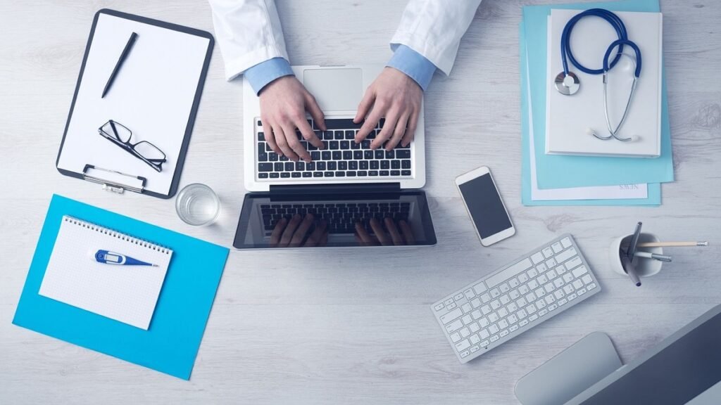 Clinician's desk with a laptop, stethoscope and clipboard
